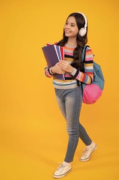 Schoolgirl, teenage student girl in headphones hold books on yellow isolated studio background. School and music education concept. Back to school. Happy teenager, positive and smiling.