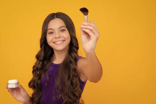 Beauty, make up and kids cosmetics. Teenage girl 12, 13, 14 years old with brush applying blush to face isolated on wellow background. Happy girl face, positive and smiling emotions