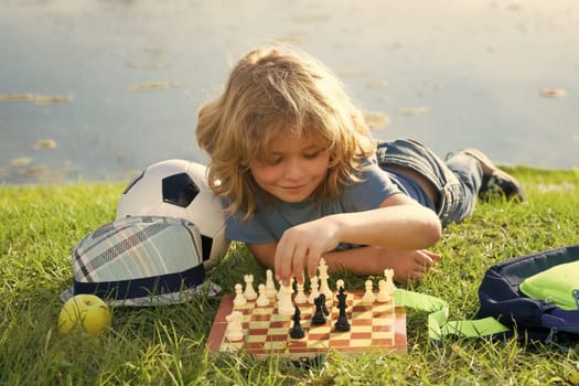 Chess school outdoor. Child think or plan about chess game, laying on grass in summer park. Intelligent, smart and clever school kids