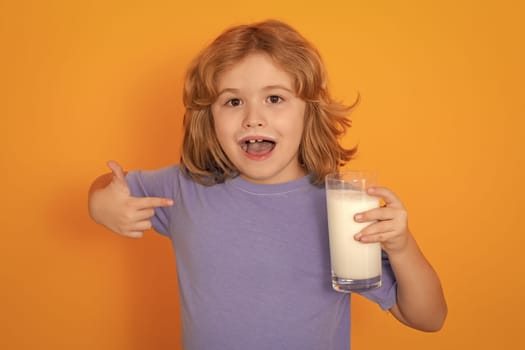 Kid boy with a glass of milk on studio background. Cute child in white shirt holding glass of milk on isolated on yellow. Portrait of kid with milk mustache