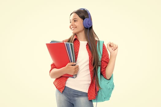 School girl, teenage 12, 13, 14 years old in headphones and books on isolated studio background. School kids with backpack. Portrait of happy smiling teenage child girl