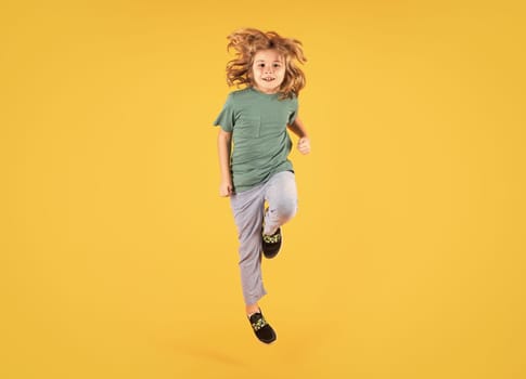 Energetic kid boy jumping and raising hands up on isolated studio background. Full length body size photo of jumping high child boy, hurrying up running fast on yellow background