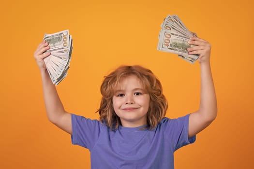 Kid showing money dollar bills, standing dreamy of rich against isolated yellow studio background