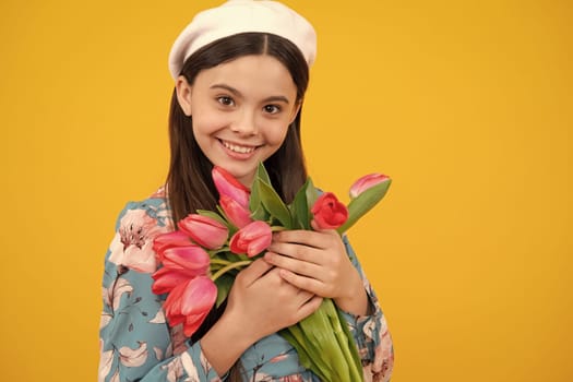 Happy teenager girl in beret hat hold spring tulip flowers on yellow background. Child with spring tulips bouquet, floral present