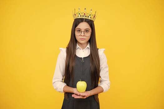 Teen child in queen crown hold apple isolated on yellow background. Princess girl in tiara. Teenage girl wear diadem