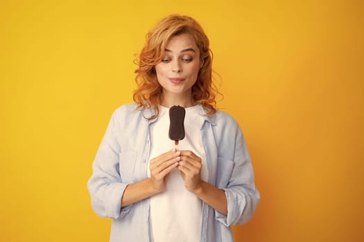 Young woman eats delicious ice cream, enjoys frozen dessert, dressed in casual clothes, isolated on yellow background