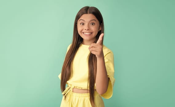 amazed child with long hair pointing finger on blue background, advertising.