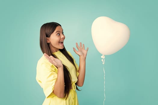 Portrait of a cute smiling teenager girl with a red heart balloon, over blue background isolated. Surprised face, surprise emotions of teenager girl