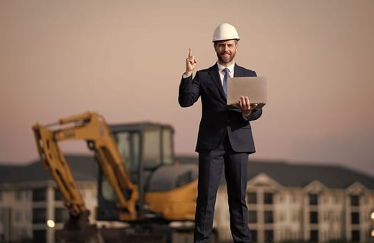 Buider man in suit and hardhat. Construction investor. Business man investor in front of construction site. Successful investor. Handsome man in suit and hardhat at building construction