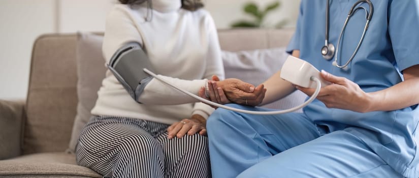 nurse doctor using digital tonometer check blood pressure for old asia female at home in elderly care cardiovascular medical visit, cholesterol problem. Home health care and nursing home concept.