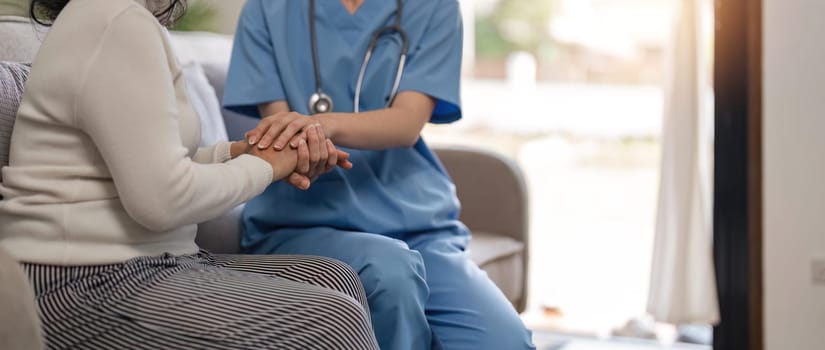 Doctor giving hope. Close up shot of young female physician leaning forward to smiling elderly lady patient holding her hand in palms. Woman caretaker in white coat supporting encouraging old person.