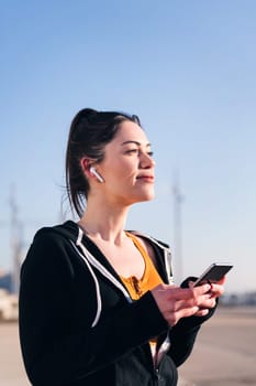 vertical portrait of a beautiful female runner playing music on mobile phone using earphones, concept of technology and sportive lifestyle
