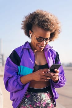 vertical portrait of a cool african american female runner playing music on mobile phone using earphones, concept of technology and sportive lifestyle