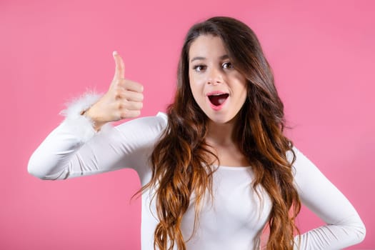 Portrait of brunette female customer with a broad smile and exciting emotions, showing thumbs up on the pink background
