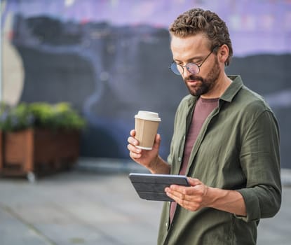 Man enjoying a coffee break outdoors while reading information from his tablet PC. The relaxed and serene atmosphere complements the combination of coffee and digital communication. . High quality photo