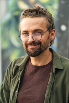 Handsome individual wearing glasses, situated outdoors against a graffiti-covered background. With a stylish and confident appearance, the subject exudes a modern and trendy vibe. . High quality photo