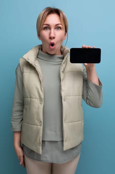 surprised 30s young blond woman in casual style holding smartphone with advertising space.