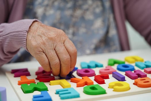 Asian elderly woman playing puzzles game to practice brain training for dementia prevention, Alzheimer disease.