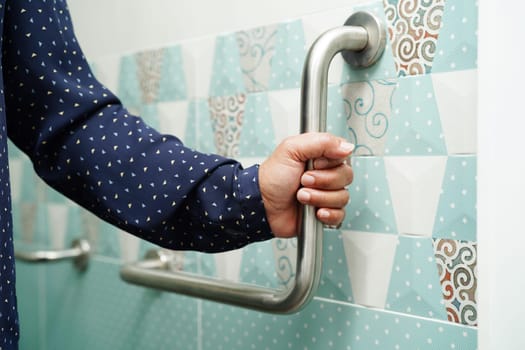 Asian woman patient use toilet support rail in bathroom, handrail safety grab bar, security in nursing hospital.