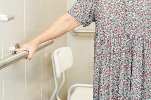 Asian elderly old woman patient use toilet support rail in bathroom, handrail safety grab bar, security in nursing hospital.