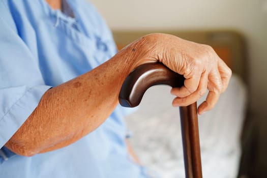 Asian elderly disability woman patient holding walking stick in wrinkled hand at hospital.