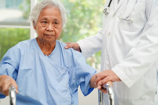 Doctor help Asian elderly woman disability patient walk with walker in nursing hospital, medical concept.