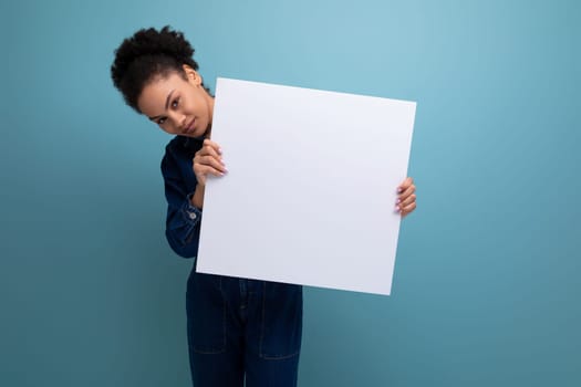 young brunette latin woman dressed in blue denim overalls holding a white board with a mockup for advertising.