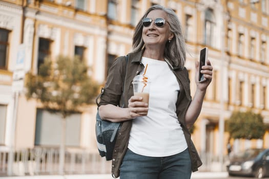 concept of travel in old age, featuring mature woman enjoying trip in old city of Europe. senior woman seen appreciating view of city and capturing moment by taking photos on mobile phone. High quality photo