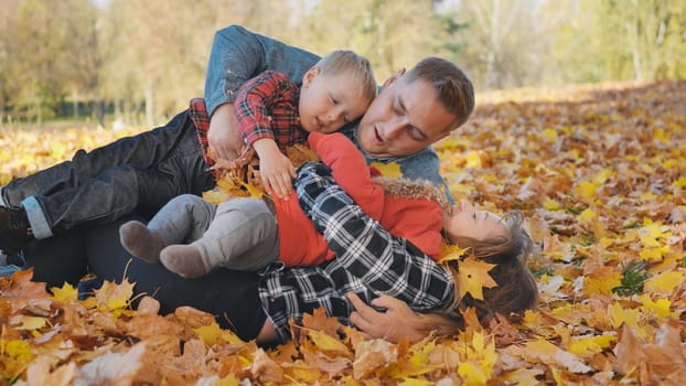A happy family in an autumn park having fun and crumbling leaves