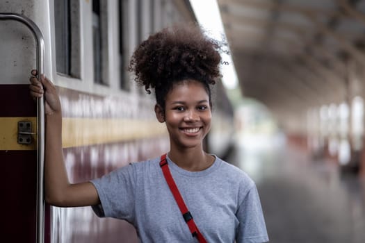 Traveler African Asian American woman getting in a train to hop on train, Young woman female standing on train door peeking out looking from door, tourist on a train station. High quality photo
