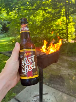 MADISON WISCONSIN, JULY 20 2023: Bottle of locally brewed Potosi Root beer in front of a fire at Devils Lake National Park in Wisconsin summer. High quality photo