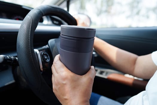 Asian woman driver hold thermo mug with hot coffee in car, dangerous and risk an accident.