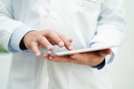 Asian man doctor using tablet computer to reading patient report, check up and search for solve treatment health medical online in hospital.