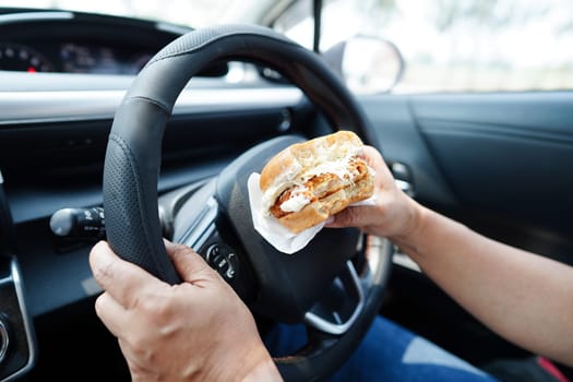 Asian woman driver hold and eat hamburger in car, dangerous and risk an accident.