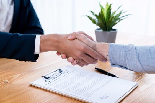 Two business people shake hand after successfully signing contract agreement in corporate office with legal document and pen on the table symbolizes business partnership and cooperation. Entity