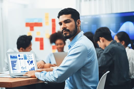 Portrait of happy and smiling businessman with group of coworkers on meeting with screen display business dashboard in background. Confident office worker at team meeting. Concord