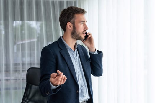 Hardworking businessman stand confidently in modern office making persuasive sales call to client. Office worker talking on the phone coordinate and manage business work with colleagues. Entity