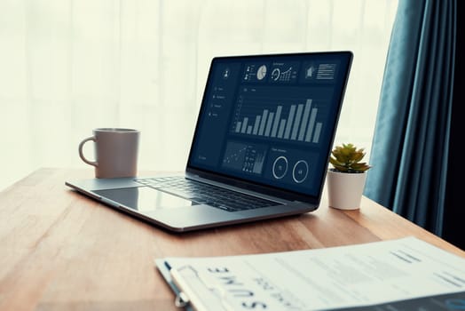 Wooden desk in office with laptop displaying Fintech dashboard business data. Business intelligence tool enhances workspace for analysts. Top view of the wooden tabletop in office. Enthusiastic