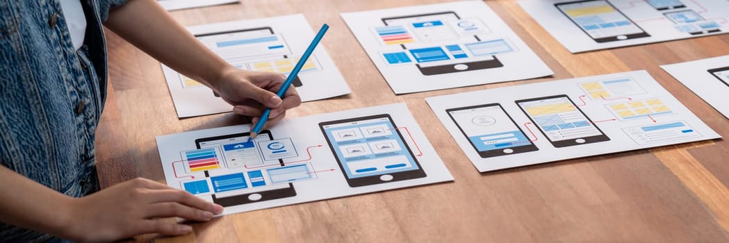 Panorama shot of front-end developer team brainstorming UI and UX designs for mobile app on paper wireframe interface. User interface development team planning for user-friendly UI design. Scrutinize