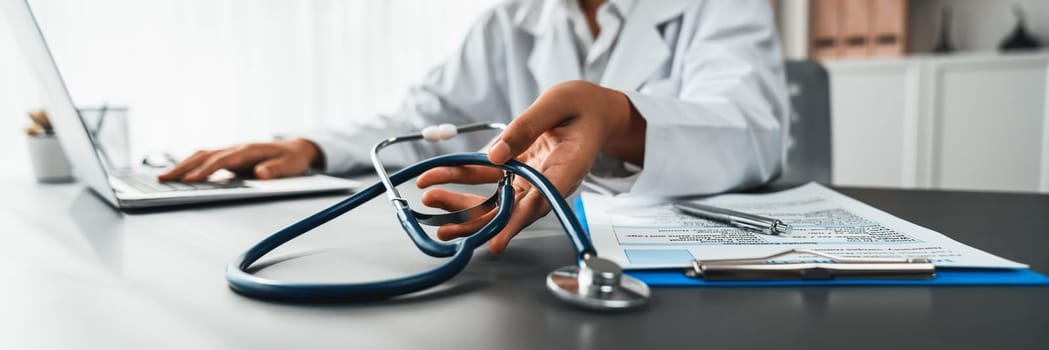 Focus stethoscope on doctor office with blurred background of doctor reviewing medical report and diagnosing illness for effective healthcare treatment plan for patient. Neoteric