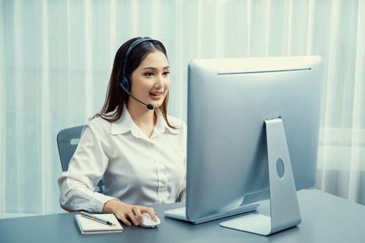 Asian call center with headset and microphone working on her laptop. Female operator provide exceptional customer service. Supportive call center agent helping customer on inquiry. Enthusiastic