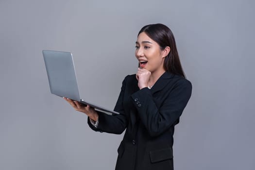 Confident young Asian businesswoman posing with laptop on isolated background. Office lady make hand holding gesture for promotions sales, technology advertisements or HR recruitment image. Jubilant