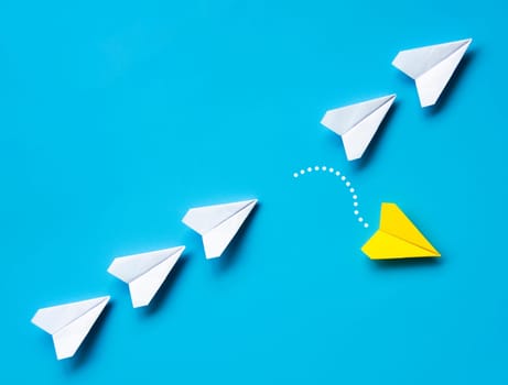 Yellow paper airplane origami leaving other white airplanes on blue background with customizable space for text or ideas. Leadership skills concept and copy space.