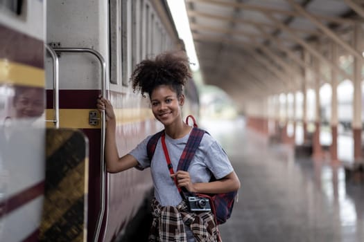 Traveler African Asian American woman getting in a train to hop on train, Young woman female standing on train door peeking out looking from door, tourist on a train station. High quality photo