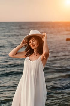 woman sea sunset. A woman in a dress, hat and with a straw bag is standing on the beach enjoying the sea. Happy summer holidays.