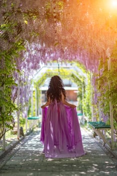 Woman wisteria lilac dress. Thoughtful happy mature woman in purple dress surrounded by chinese wisteria.