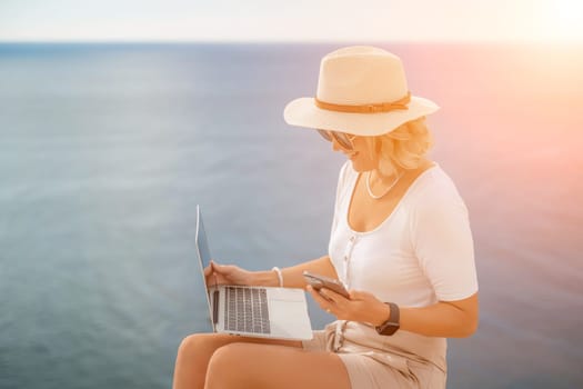 Freelance women sea working on the computer. Good looking middle aged woman typing on a laptop keyboard outdoors with a beautiful sea view. The concept of remote work