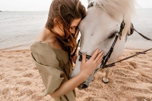 A white horse and a woman in a dress stand on a beach, with the sky and sea creating a picturesque backdrop for the scene