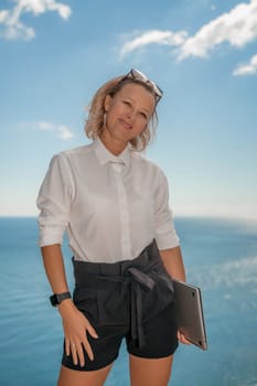 Freelance women sea working on a computer. Pretty middle aged woman with computer and phone outdoors with beautiful sea view. The concept of remote work