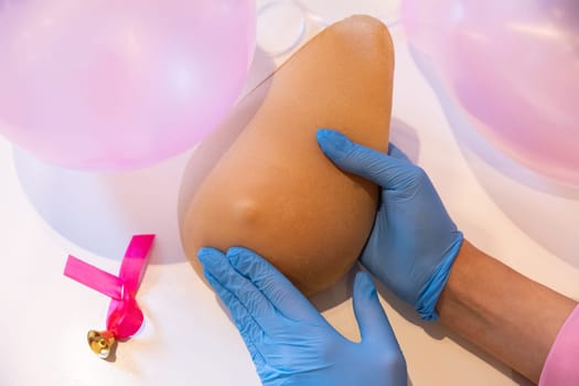 Instruction on how to compress your breast with one hand on the phantom of Lady M. Professional demonstration of the technique of examining your own breast. Pink balloons in the background.